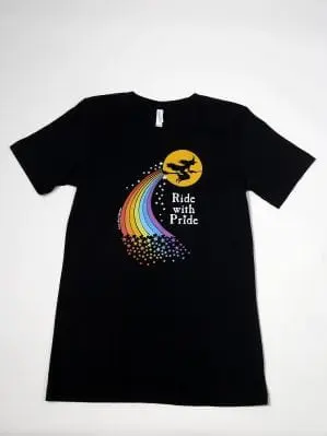 Black t-shirt printed with the words "Ride with Pride" and a witch flying across a yellow moon, trailing rainbow stars