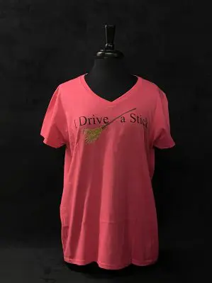 Image of Pink v-neck style women's fit t-shirt. The pattern on the front is of an illustrated broomstick with text reading 'I Drive A Stick.'