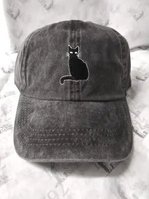 A front facing view of a grey baseball hat. Has a black cat embroidered on the front. It is sitting and has white eyes.