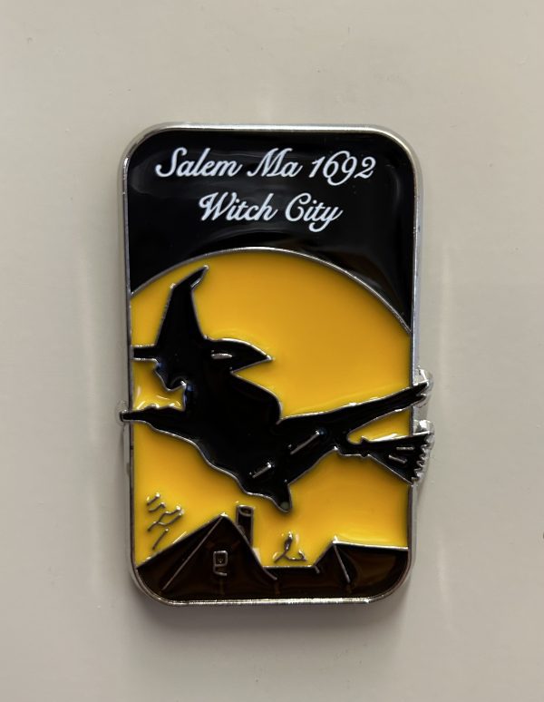 Acrylic Salem witch magnet. A black silhouette of a witch flying in front of a yellow moon. She is flying over a colonial house. Text above the witch reads "Salem 1692 Witch City".