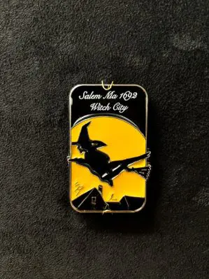 Yellow and black magnet with witch flying over colonial buildings.