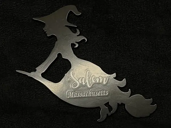 Image of a magnet featuring a silhouette style witch flying on a broomstick. The space between the witch's skirt and arm is functional as a bottle opener. Overlaid on the witch's skirt are the words "Salem, Massachusetts" written in a cursive font.