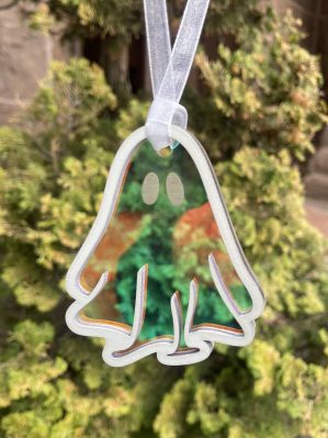 A simple, yet attractive ornament with a wooden outline of a cartoony bedsheet ghost backed by translucent, iridescent piece of acrylic. The suncatcher hangs from a piece of white shiny ribbon.